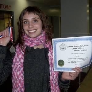 Aquí hay una mujer joven rubia sonriente que sostiene un diploma en su mano y en la otra una medalla