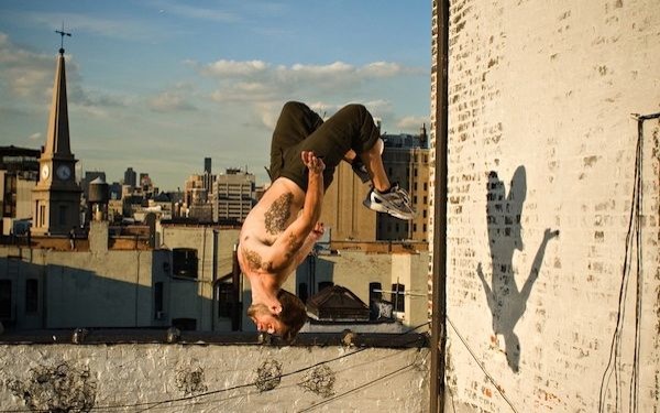 Un hombre en el techo de una ciudad en la mitad del aire de cabeza