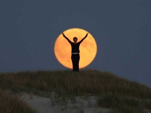 Una persona de pie alzando sus brazos parece estar parado con luna detras
