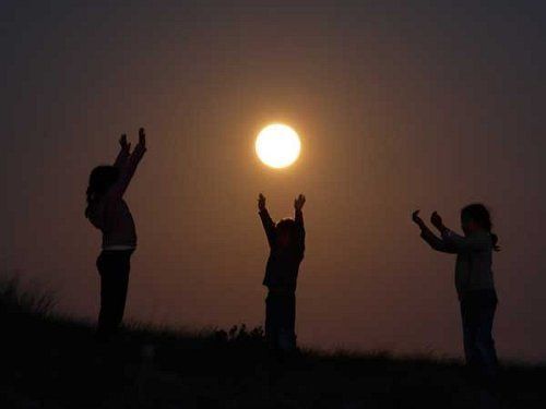 Observamos tres niños en una noche de luna que juegan levantando las manos hacia ella