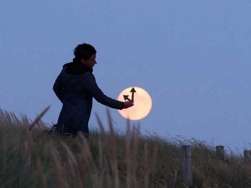 UN hombre en una noche muy clara coloca unas flechas que parecen colocarle la hora dentro de la luna