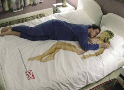 Hay un hombre acostado en su cama  sobre su cubrelecho que simula estar al lado de una mujer pero ella esta es pintada ahi