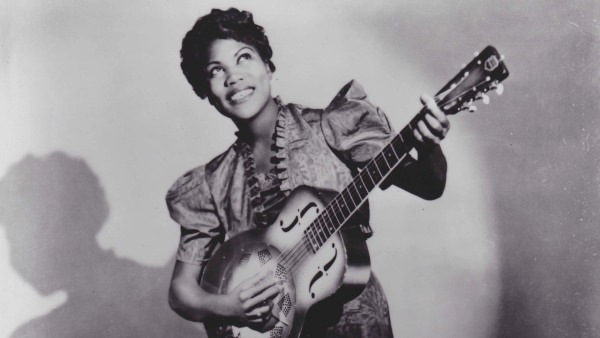 Una mujer tocando una guitarra de lado con una gran sonrisa mirando hacia arriba