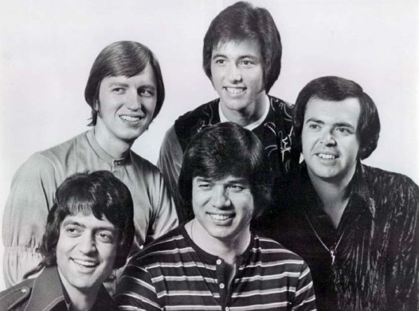 Un grupo de cinco jóvenes, todos con una sonrisa y corte de pelo de los sesenta 