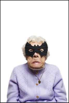 vemos auna mujer mayor con su sweter color lila y hace una expresión  con su boca y lleva un antifaz de batman