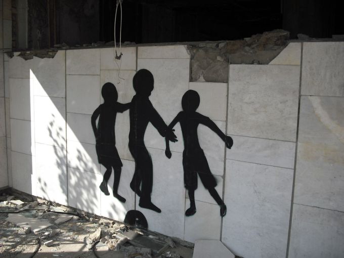 Vemos un gaffiti sobre una pared que muestra tres personas de la mano en color negro y el piso esta agrietado