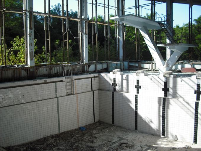 Vemos una piscina sin agua acabada la baldosas reventadas  vemos escaleras  y mucho mas de la estructura 