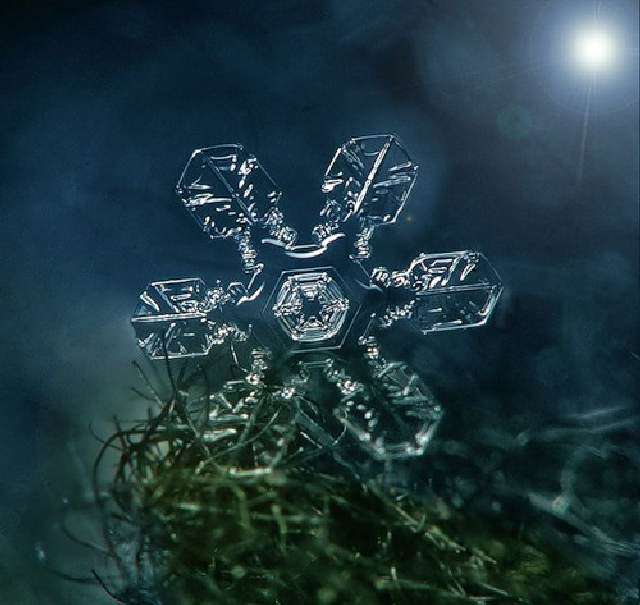 Un copo de nieve con una forma cruz pequeña con seis puntas y un parte central muy brillante