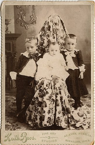 Vemos a tres niños dos niños y una niña que posan elegantes en sus trajes de epoca para una foto