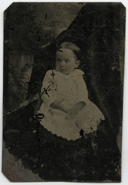 Una niña con traje blanco sentada sobre una alfombra mira al  frente fijamente 