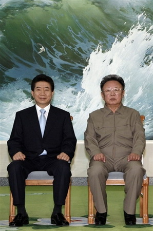 Dos hombres de raza oriental uno junto al otro y detrás una foto  de un mar con olas