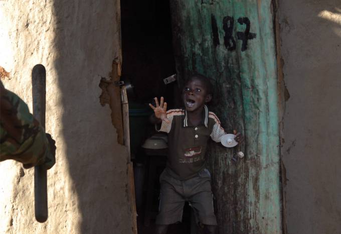 Un niño africano muestra cara de terror cuando al abrir la puerta de su casa ve aun policía  con un arma en su mano