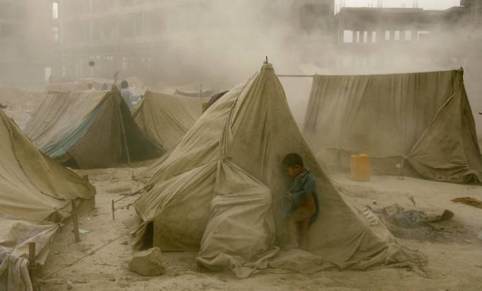 Un niño se esconde  detrás de una carpa en el desierto mientras pasa una tormenta de arena