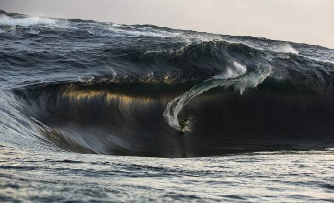 Vemos a una persona que hace surfing y  una inmensa ola  que esta llegando
