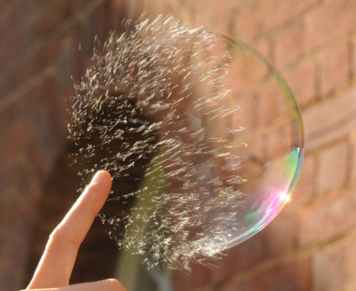 Tenemos una burbuja de jabón  con unas pequeñas  partículas y un dedo  que la toca susvemente