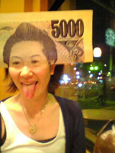 Observamos acá una mujer sacando su lengua donde su rostro se completa con un billete que presenta un rostro oriental 