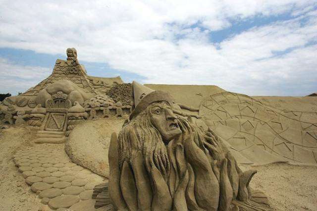 Vemos en una colina un castillo hecho en arena junto con unas figuras muy raras con cra de mujer