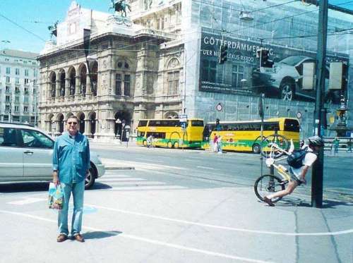 Un cruze de calles dos buses amarillos en una esquina un hombre de azul posa  para una foto y en el poste otra persona  se recuesta  en su  biciceta