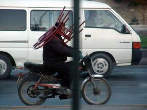 Un hombre lleva una silla encima de su cabeza mientras maneja su moto