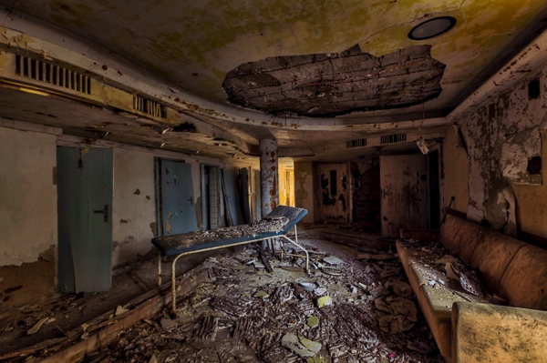 Un cuarto muy feo y lleno de escombros en el cual hay una cama de hospital en el medio