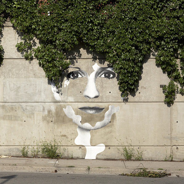 Una cara en la cual el pelo son ramas verdes que caen por el muro