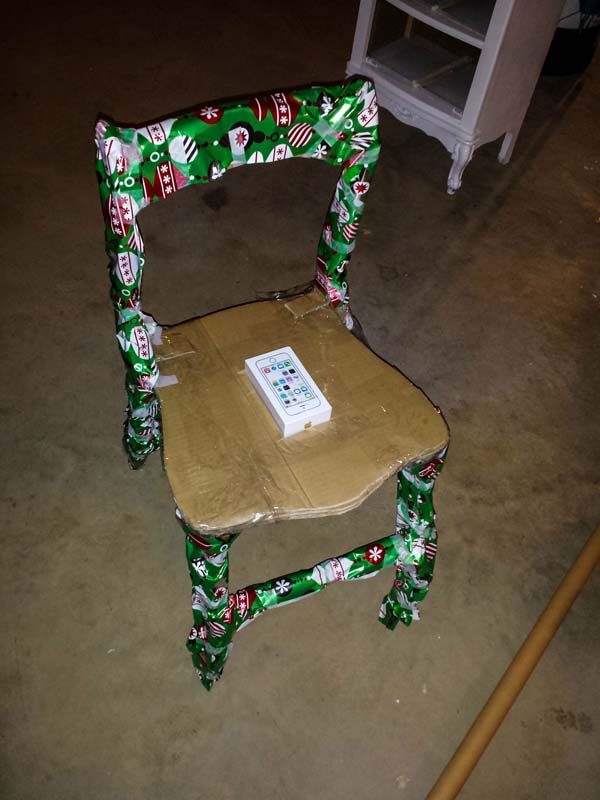 Vemos ahora la misma silla que sigue envolviendose en papel navideño verde y en la parete se sentarse ahora reposa el celular
