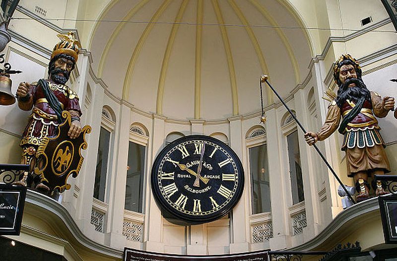 Foto a un reloj muy grande y dos esculturas a sus lados