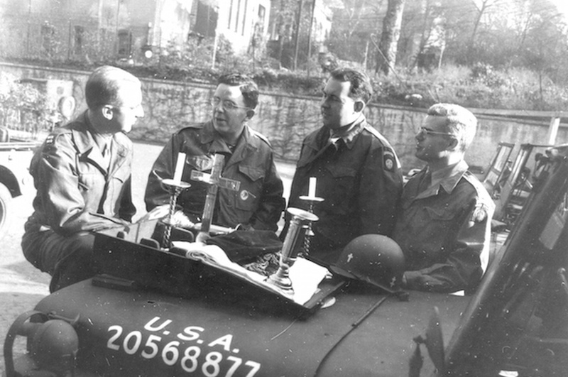 Cuatro capellanes militares charlando sobre un Jeep Willys 