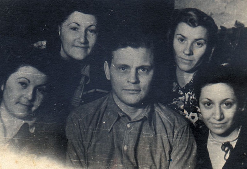 Cuatro mujeres y un hombre en el centro miran hacia la cámara mientras les toman una foto.