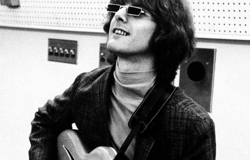 Un músico con guitarra y lentes negros mira hacia arriba en un estudio