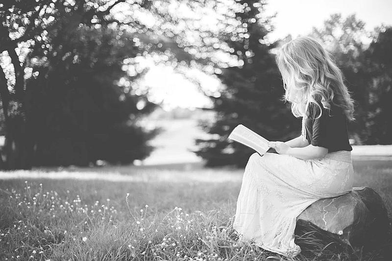 Una mujer joven en medio de la naturaleza  lee un libro muy tranquila