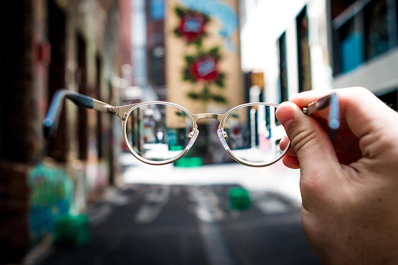 Vemos calles a  ambos lados y una persona que sostiene unas gafas de lentes blancas