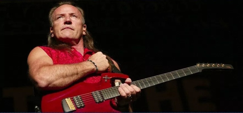Un hombre rubio con camisa roja sin mangas y tocando su guitarra