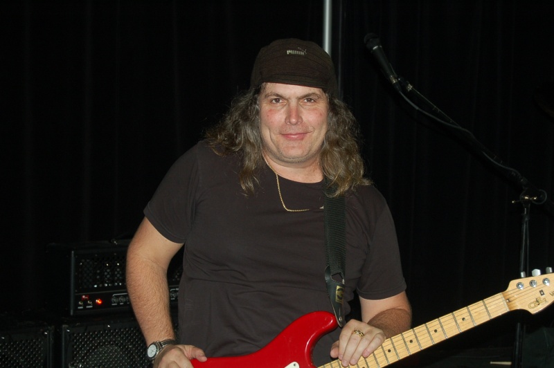 Un músico de pelo largo con su guitarra y sonriendo 