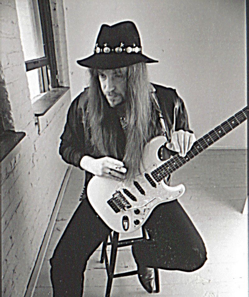 Una persona con ropa negra y sombrero negro que toca su guitarra