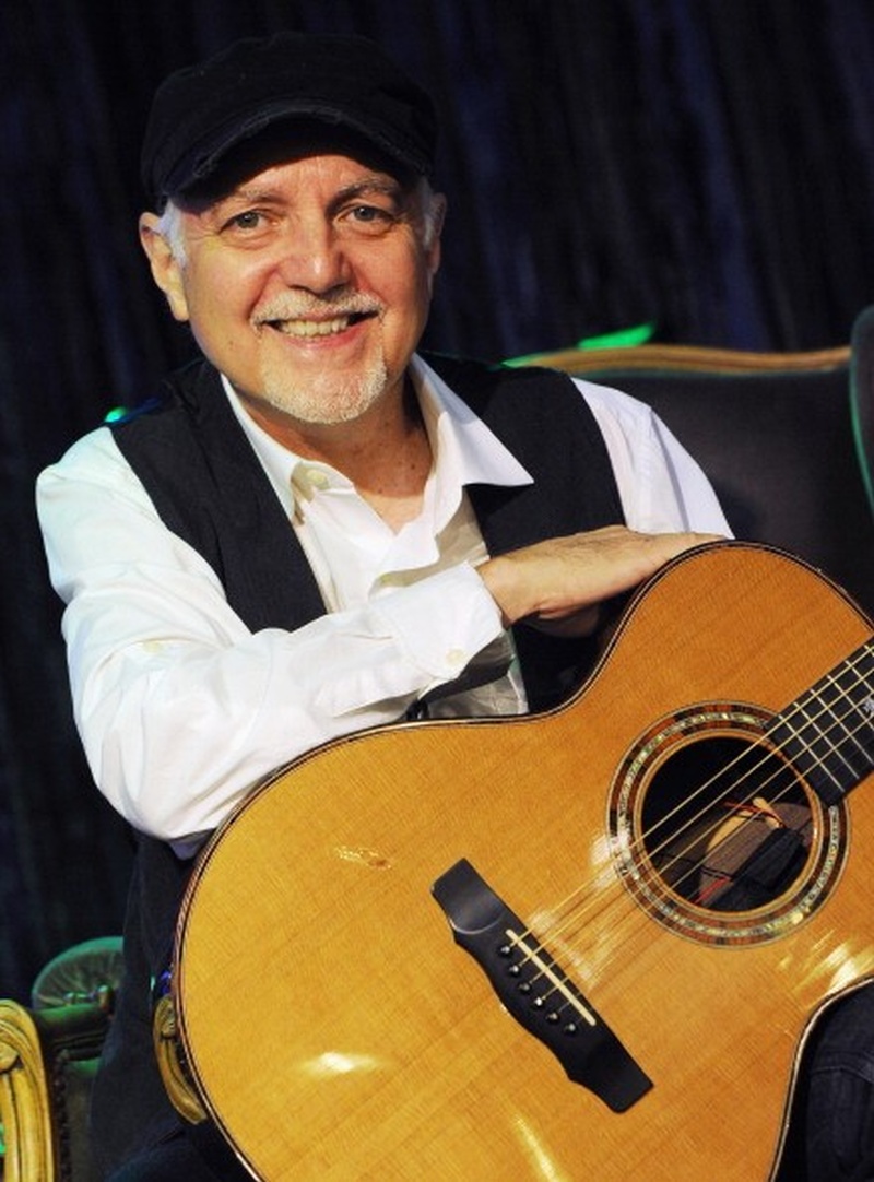Un hombre algo mayor con una gorra y una linda sonrisa y su guitarra