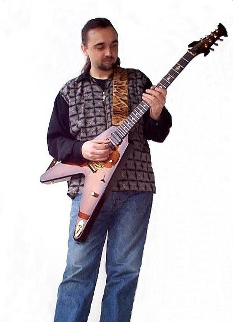 Un hombre con saco azul y sonriendo toca su guitarra