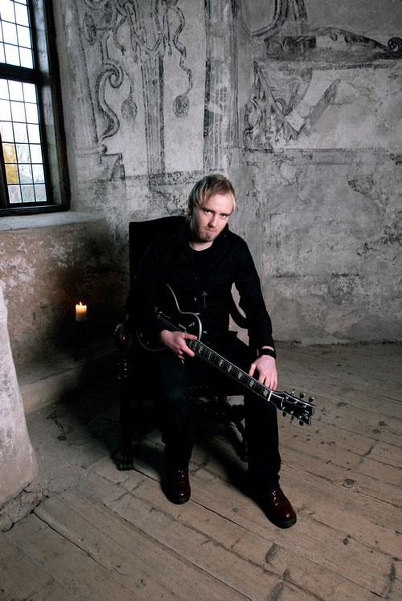 Un hombre en un lugar lúgubre con ropa negra sentado con una guitarra