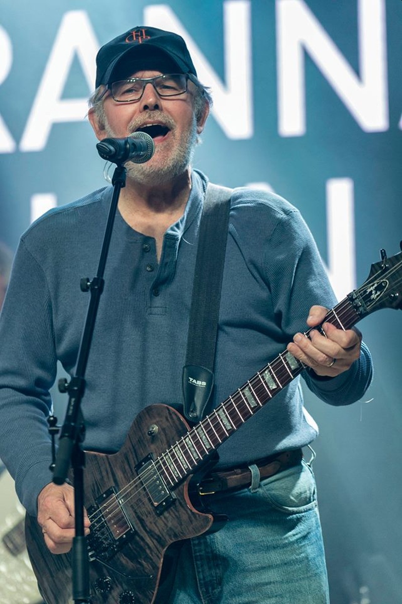Un hombre mayor con gafas y gorra canta acompañado de su guitarra