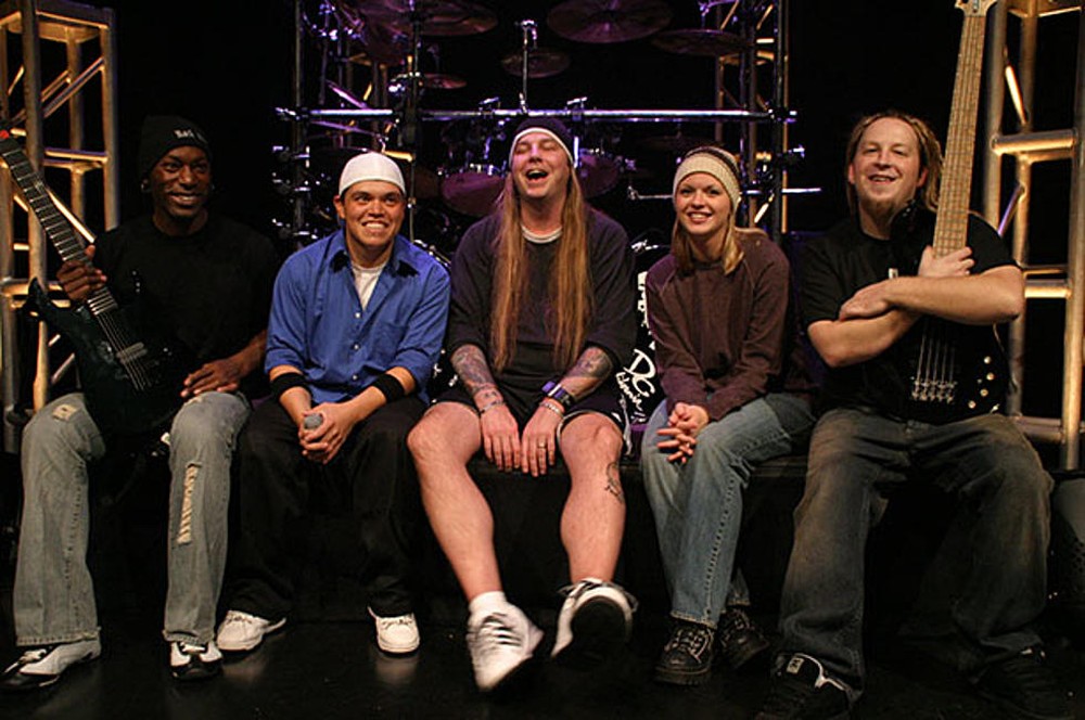 Una banda de rock sonriente sentada al lado de un escenario muy felices