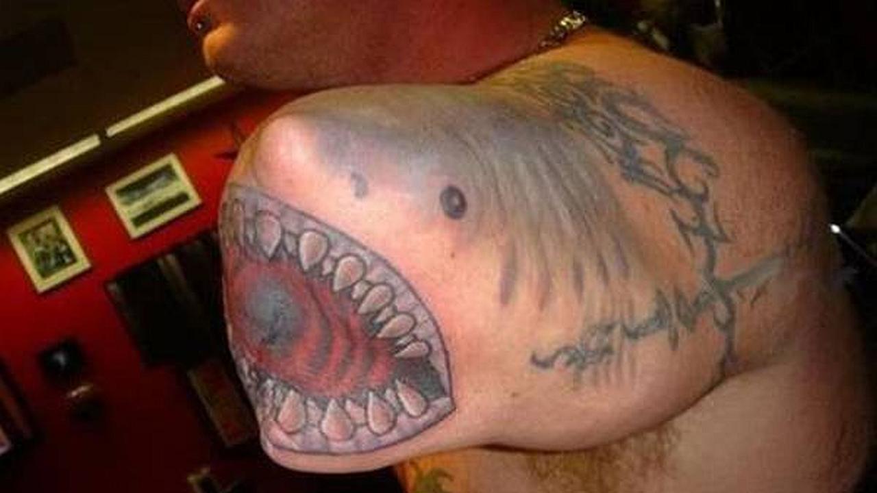 Un hombre con un tatuaje de tiburon en su codo, es como si su codo fuera el tiburón