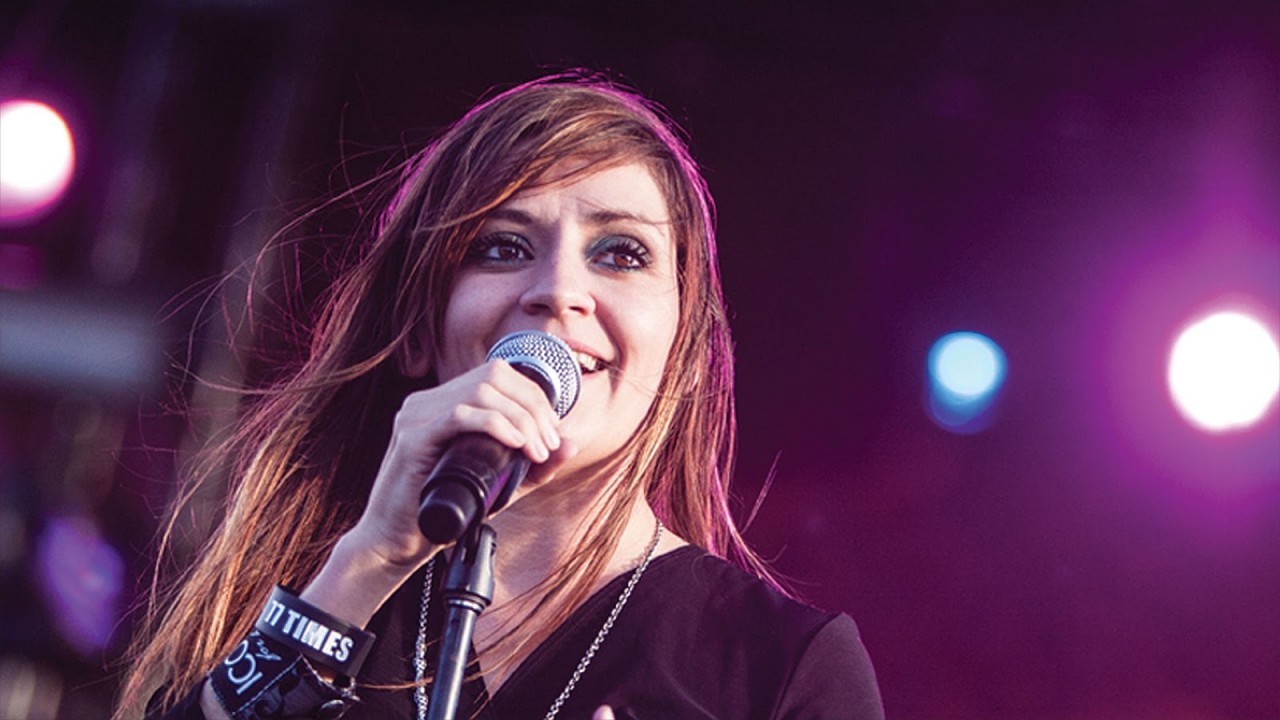 Una mujer joven sonriente rubia que canta sostiene un micrófono en sus manos