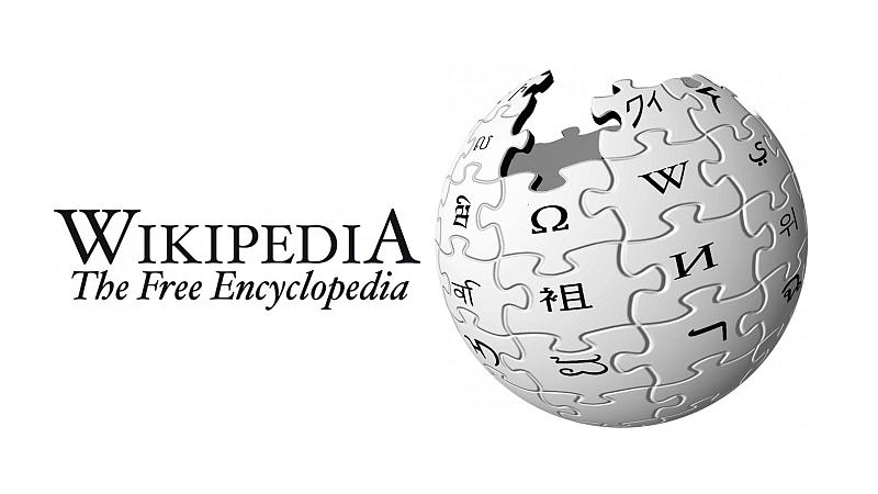 Vemos un fondo blanco con una esfera que tiene fichas de rompecabezas co letras en diferentes idiomas y la palabra wikipedia la enciclopedia libre