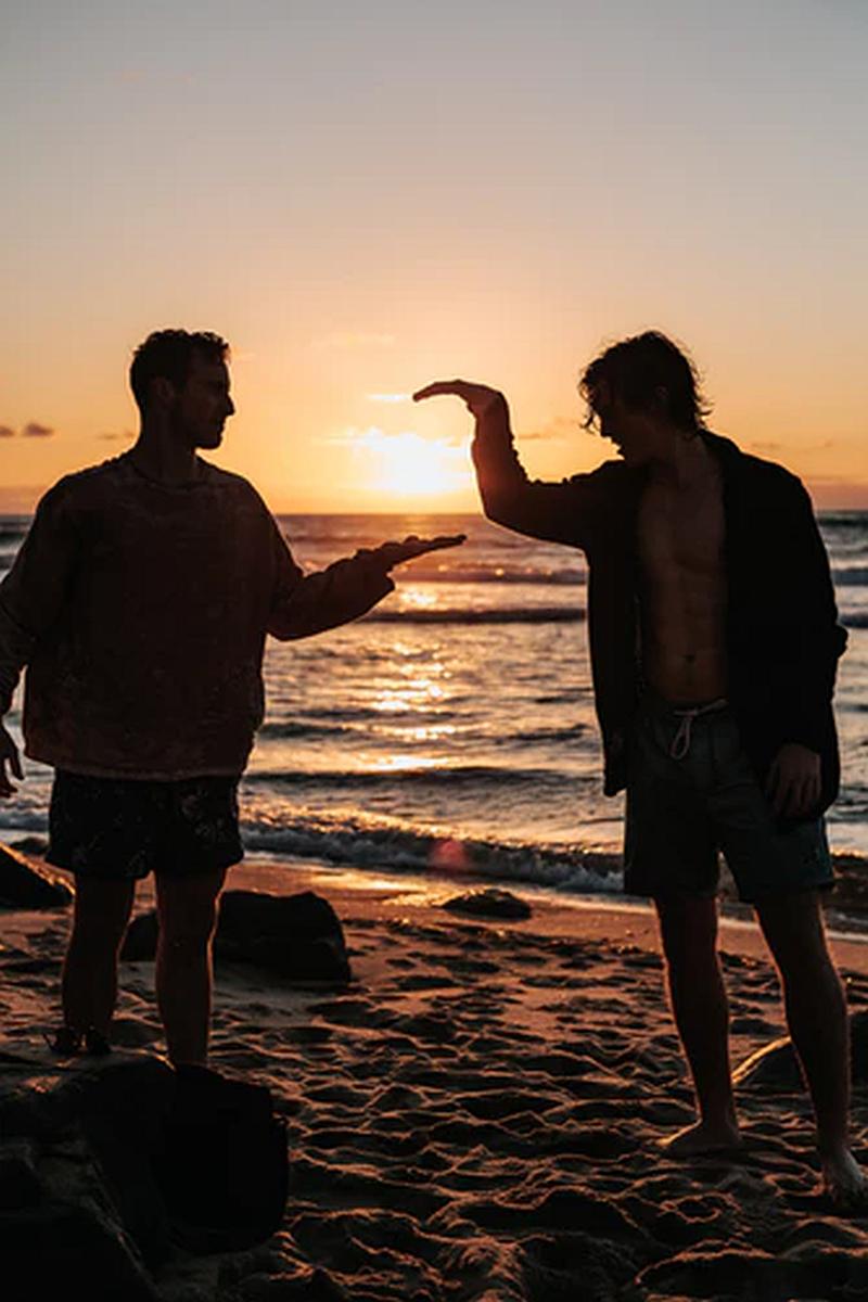 Dos amigos sobre la arena del mar la playa un atardecer se dan golpes de saludo 