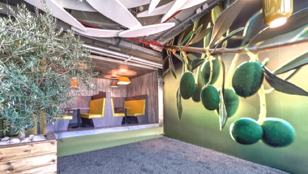 Vemos un pequeño salón con sillas amarillas para cuatro personas también vemos una matas muy verdes y en la pared se ve una pintura de frutas en su fondo