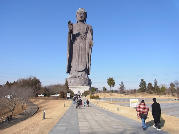 Imagen de Buda color gris sobre un pedestal bajo con una mano en posición de saludo