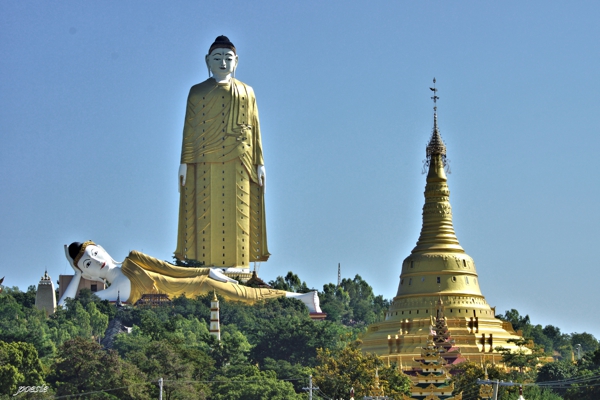 Figura gigante dorada observando a otra imagen dorada en posición de descanso al lado de una pagoda