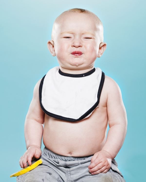 Un bebe  prueba el limón no le gusta y hace un gesto de desaprobacion