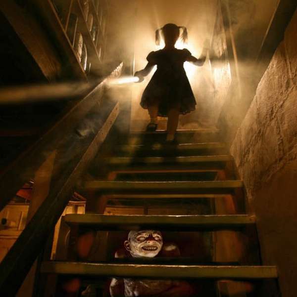 Una niña baja un sótano  algo oscuro y debajo  de la escala hay una mascara con aspecto miedoso