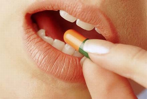 El primer plano de una boca con unos dedos insertando una píldora en ella